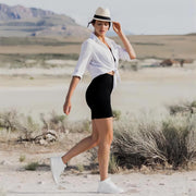 Woman in black leggings and white shirt, wearing a hat, in a desert landscape with mountains.
