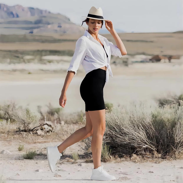 Woman in black leggings and white shirt, wearing a hat, in a desert landscape with mountains.